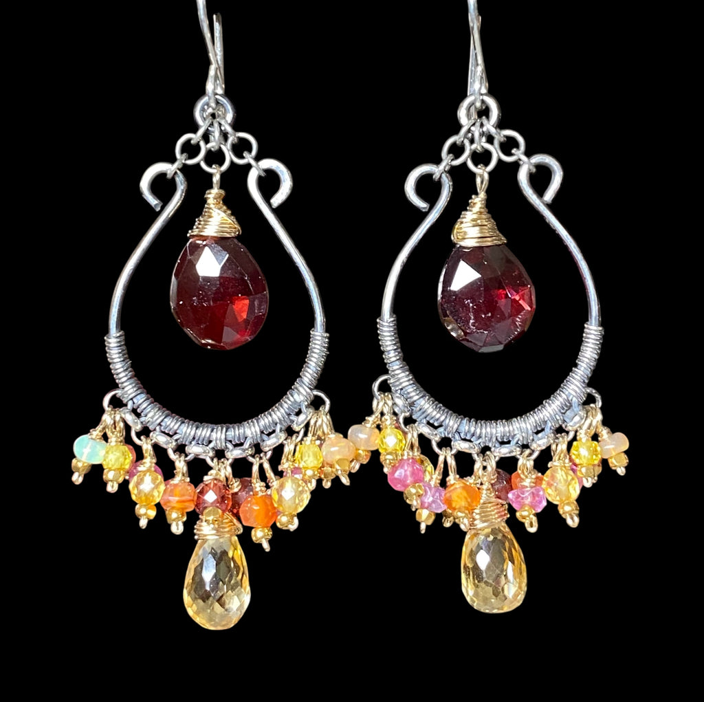 Red garnet and citrine mixed metal hoop earrings against solid black background