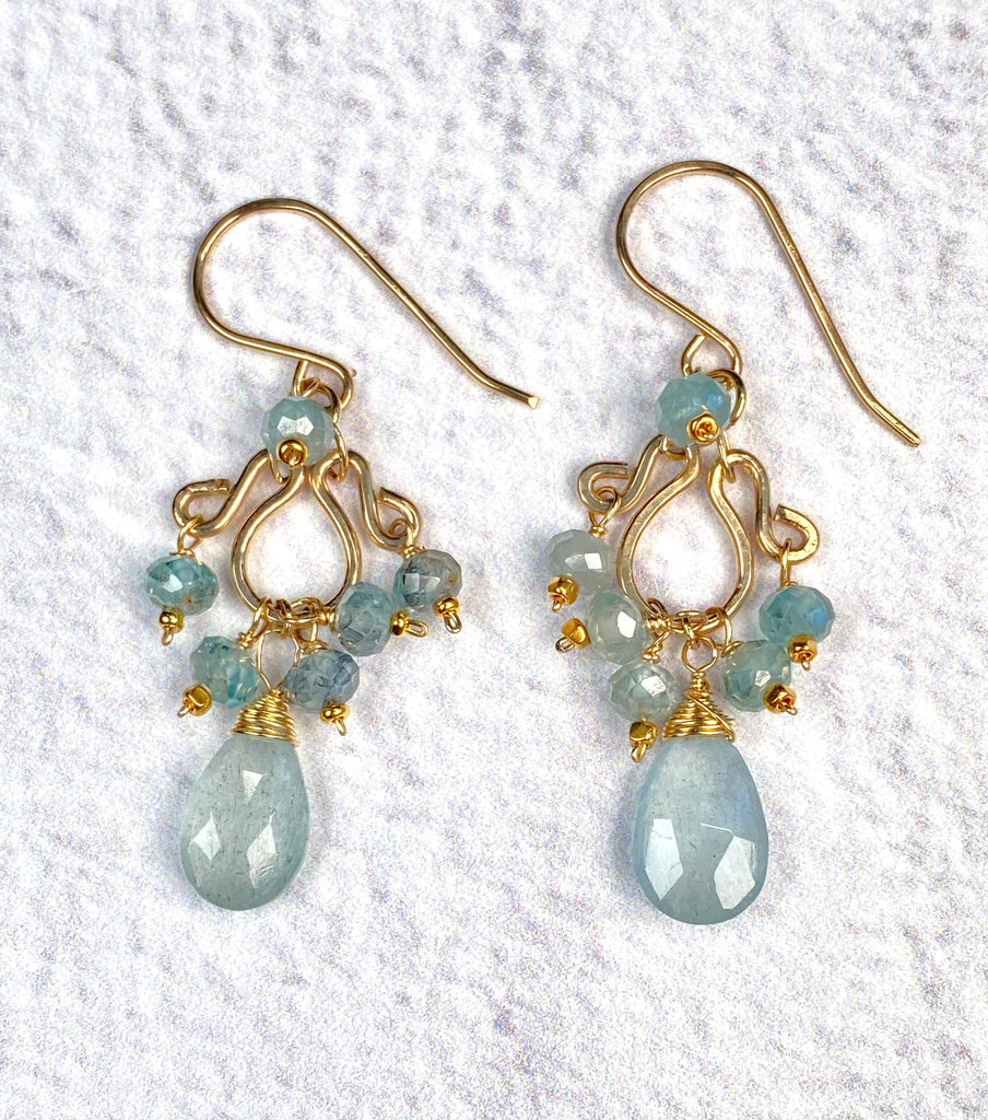 Front view of moss aquamarine and blue zircon petite chandelier earrings on white fabric, with blue bead clusters beneath open gold-filled scrollwork.