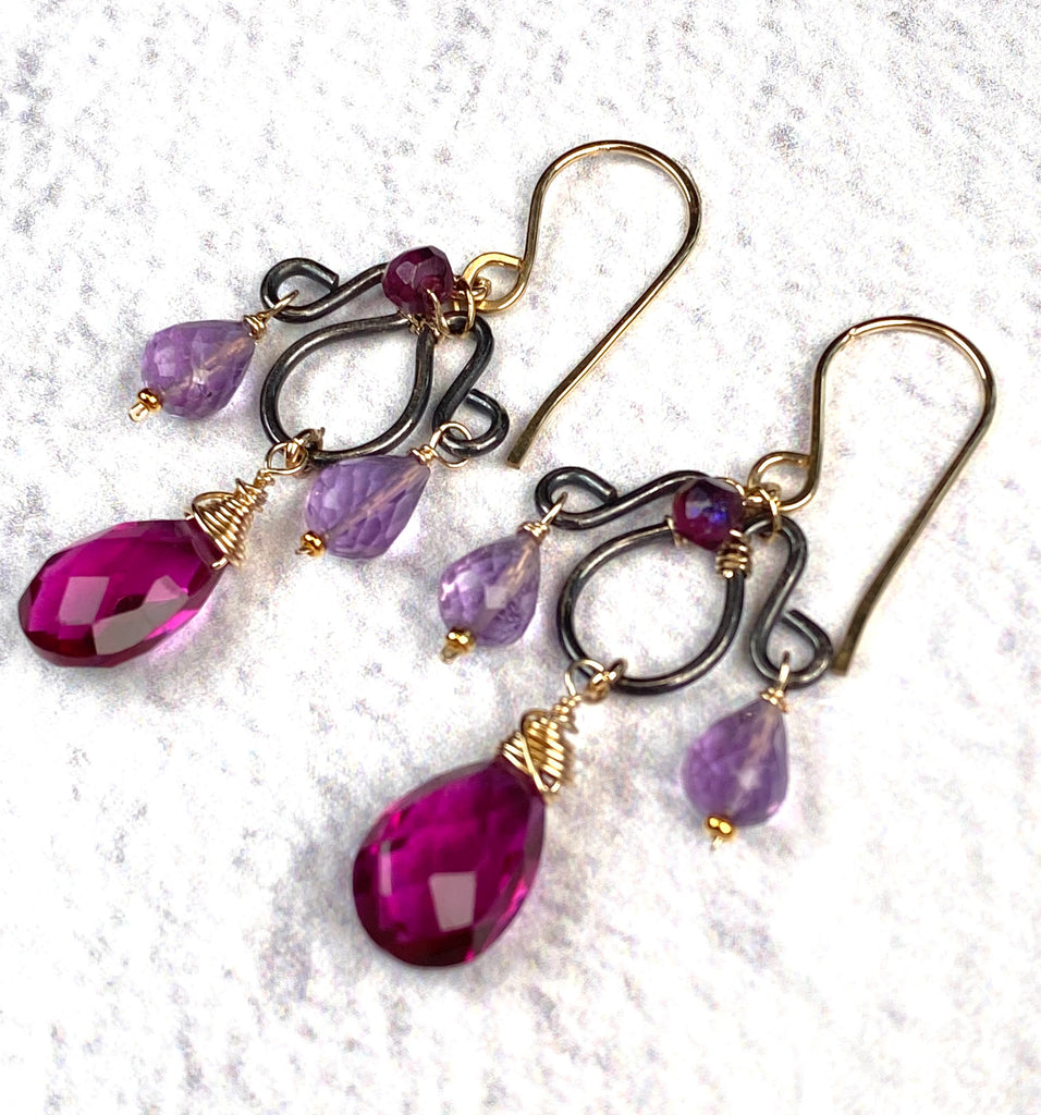 Angled view of rhodolite garnet and lavender amethyst earrings, showing almost-black sterling silver frames and gold-filled wire wrapping.