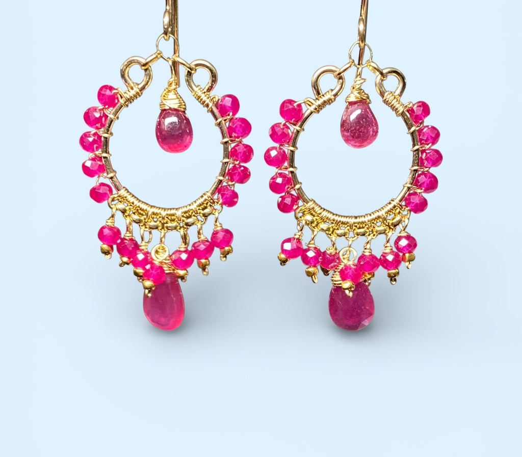 Red ruby pink sapphire gold chandelier hoop earrings dangling in front of light blue background