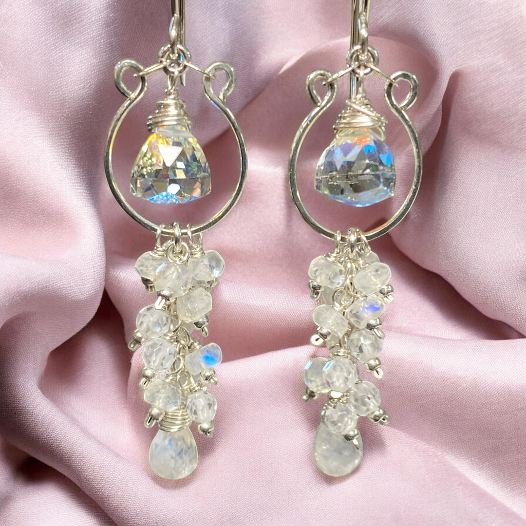 Pair of sterling silver chandelier earrings withwhite and clear gemstones on a pink fabric background.