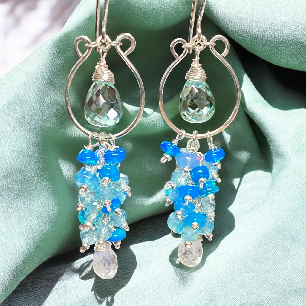 Pair of sterling silver chandelier earrings with blue and clear gemstones on a green fabric background