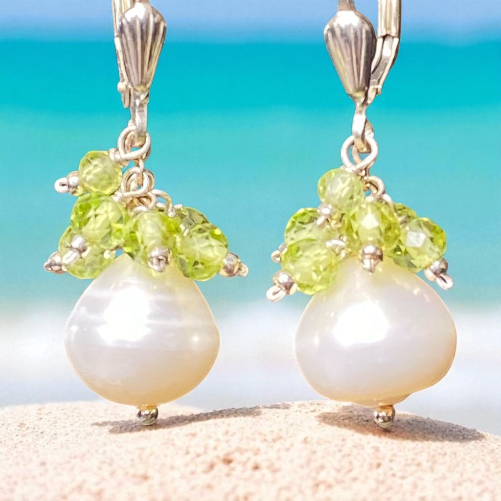 Pearl and green gemstone earrings on a beach background