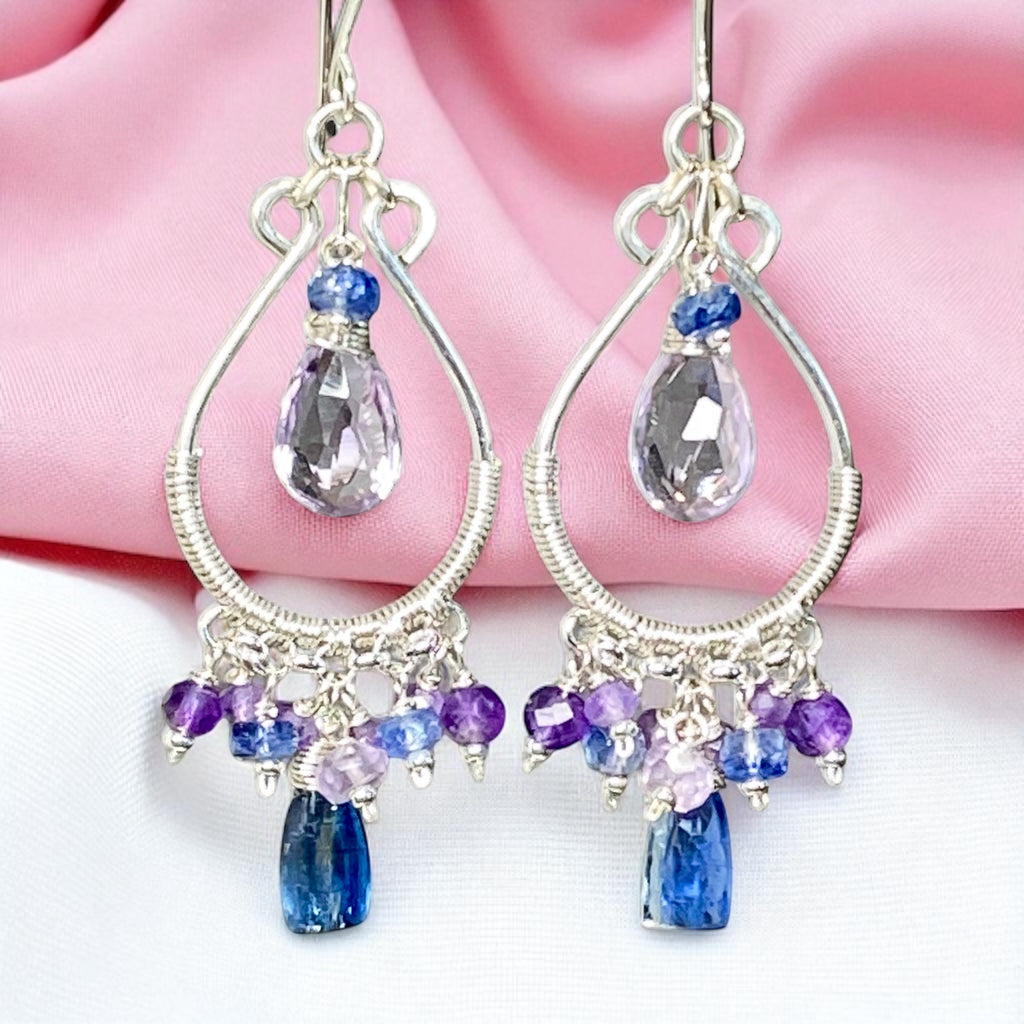 Silver earrings with teardrop-shaped gemstones on a pink fabric background