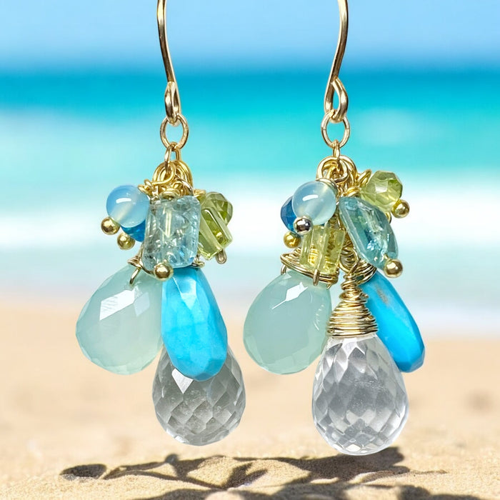Handmade turquoise, aqua chalcedony, and crystal quartz cluster earrings with gold-filled wirework against a beach-inspired background.