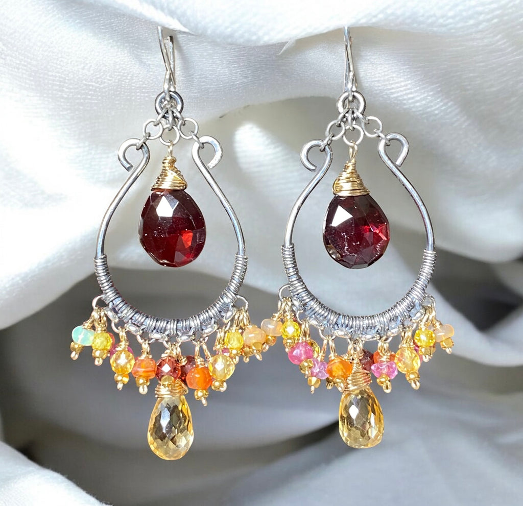 Garnet citrine mixed metal chandelier hoop earrings dangling against white draped fabric over grey surface