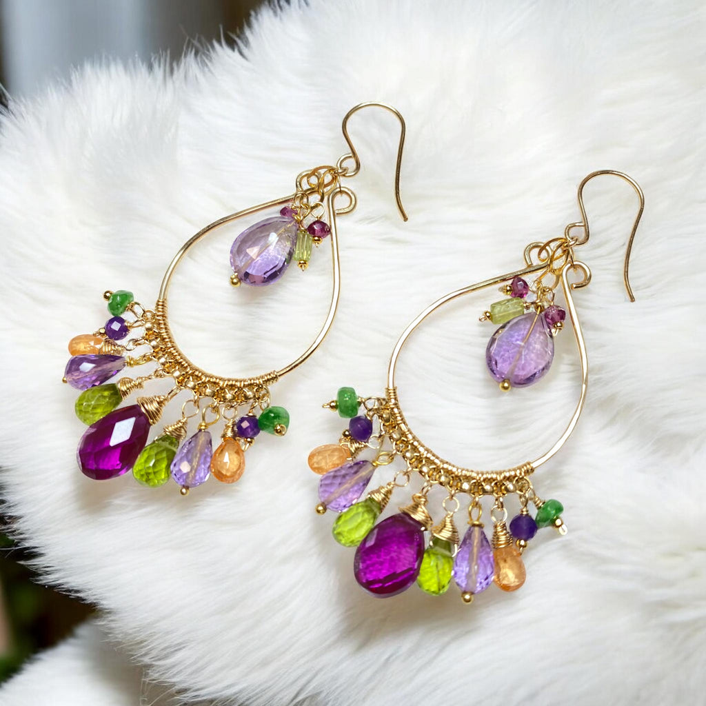 Handmade multi gemstone chandelier earrings in violet, green and pink lying on soft white furry fabric — gold fill hoops