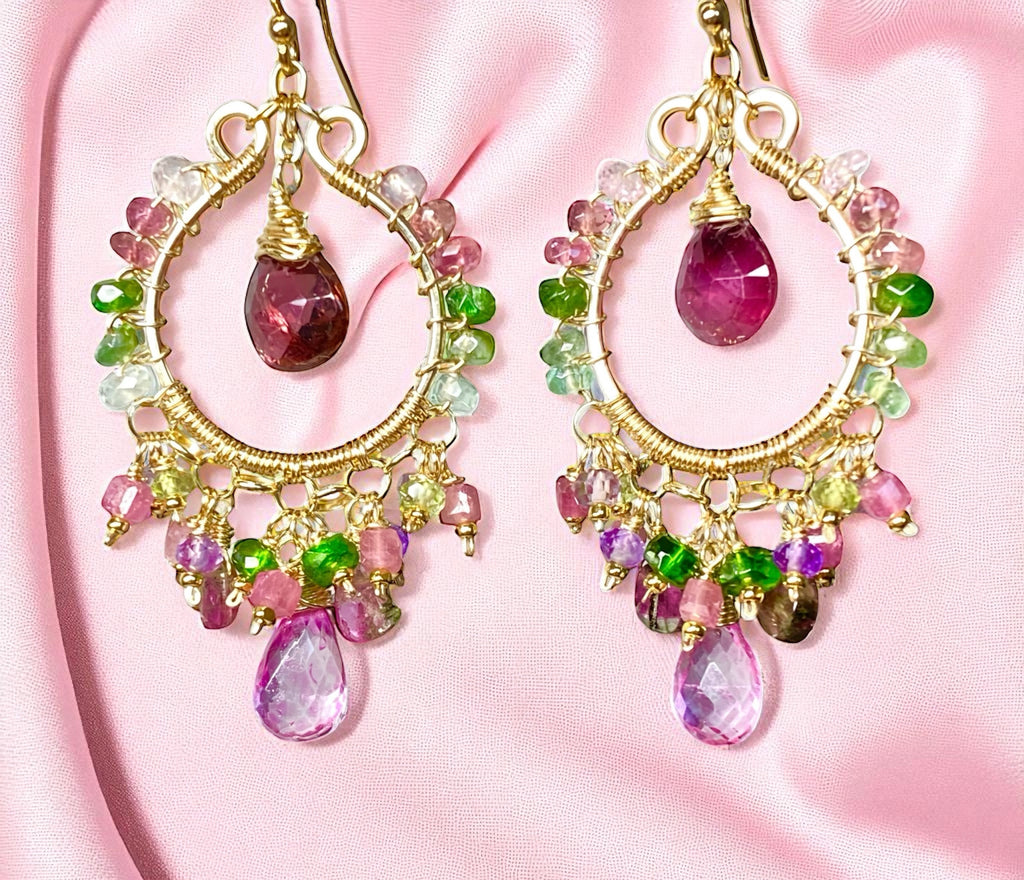 Colorful gemstone earrings with gold accents on a pink fabric background