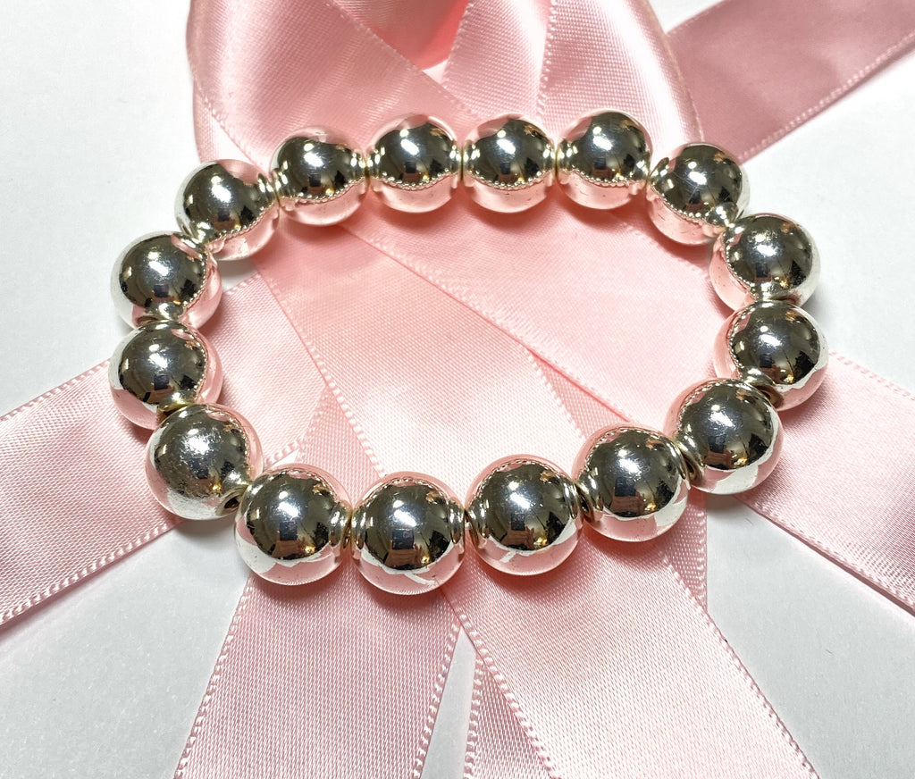Polished silver hematite bead stretch bracelet resting on pink satin ribbon, showing its circular shape and reflective finish.